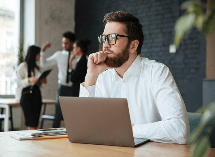 Homem sentado em frente ao notebook e pensando em idéias