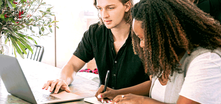 Duas pessoas sentadas em uma mesa trabalhando em um laptop